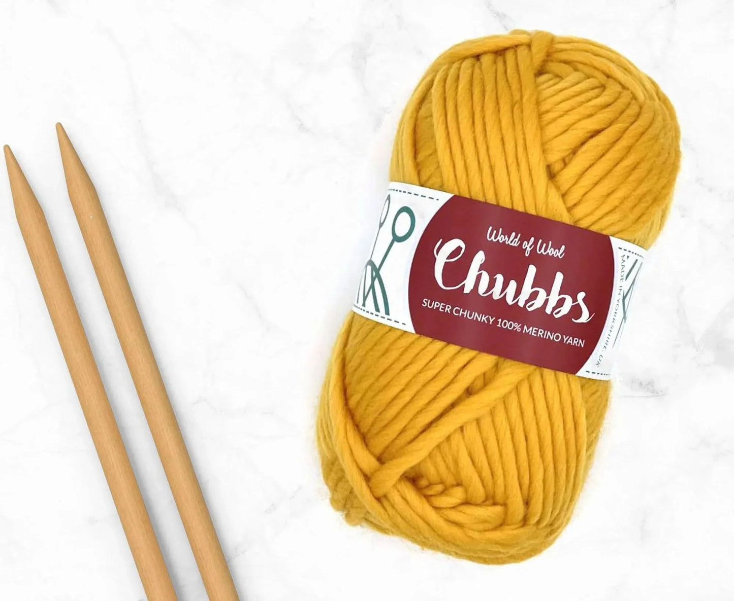 Yellow yarn ball of super chunky 100% merino wool with World of Wool 'Chubbs' label and wooden knitting needles on a white background