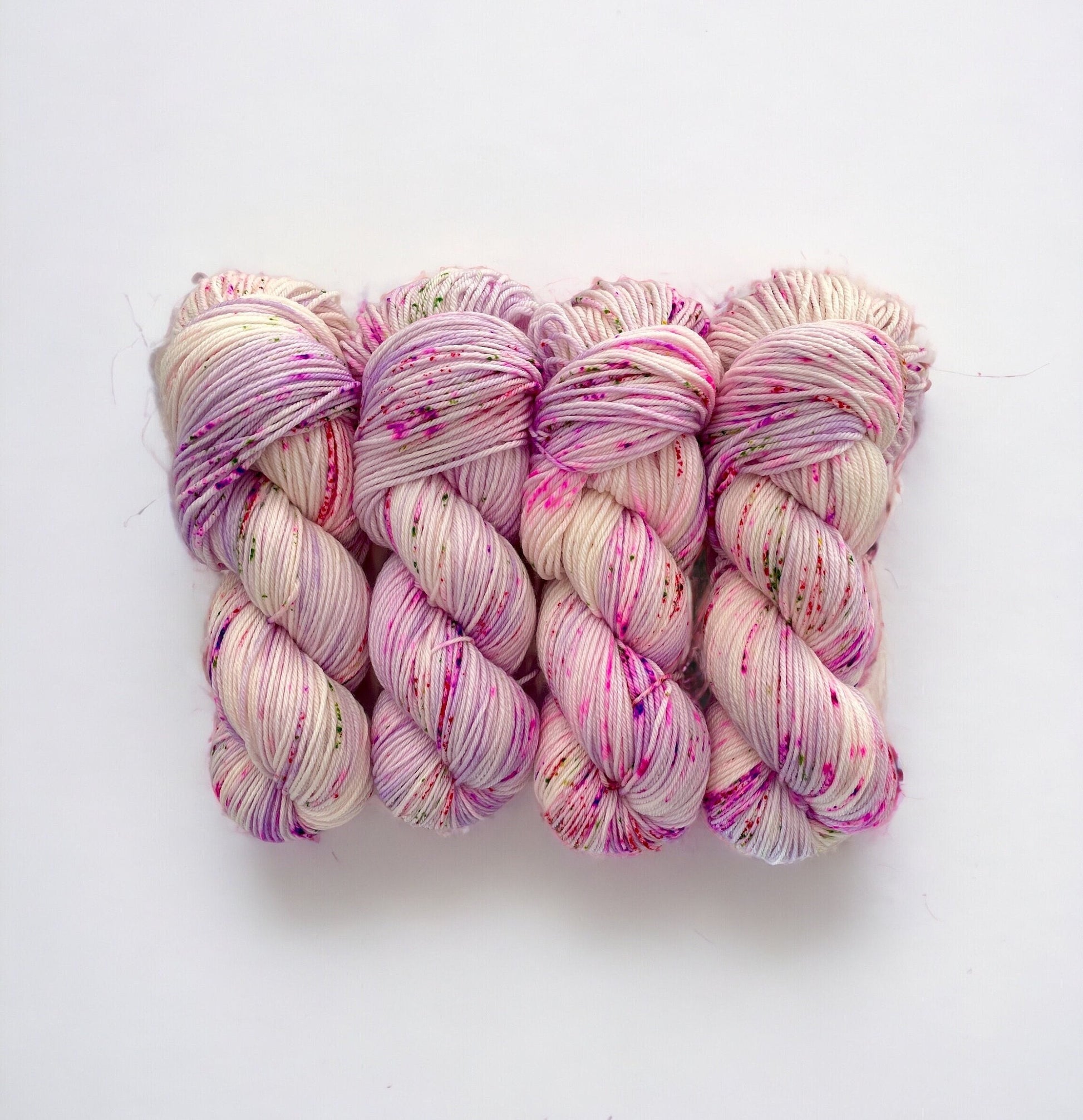 Discover the beautiful world of hand-dyed yarn with FAIRY DUST. Made from superwash merino wool and nylon, this double knit yarn is soft and durable. The white and lilac base is speckled with hints of pink and green, adding unique character to every skein. Elevate your knitting and crochet projects with FAIRY DUST.